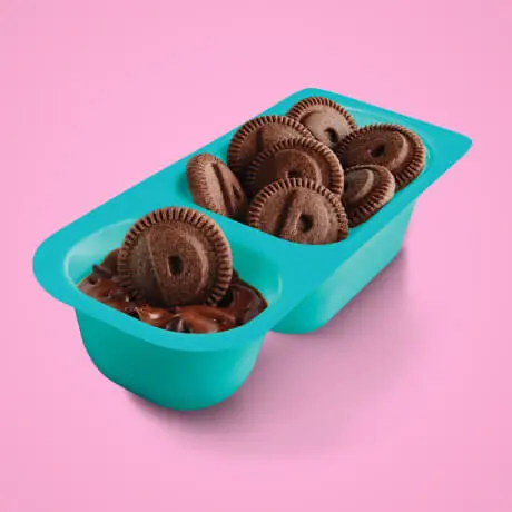 An opened snack tub of chocolate flavored Dunkaroo biscuits with chocolate dip on a pink background