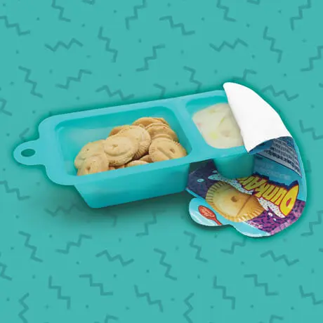 An opened snack tub of vanilla flavored Dunkaroo biscuits with vanilla rainbow sprinkle dip on a patterned teal background.
